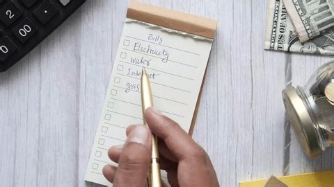 clip-4017570705-person-checking-off-bill-payments-on-notepad