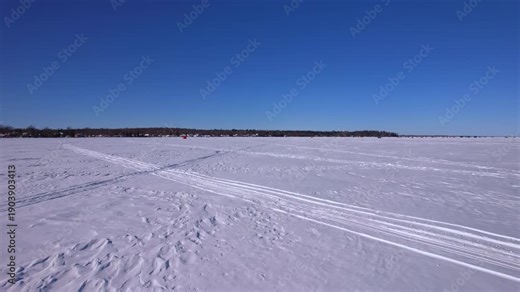 Drone footage at snowmobile atv or snowdog tracks across frozen lake surface of Simcoe lake in Cook’s Bay, Innisfil, Ontario. Winter ice fishing season charters for jumbo perch, pike, white fish.