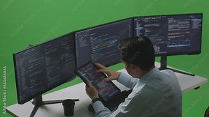 Side View Of Asian Man Developer Working With Tablet While Write Code With Multiple Computer Screens In Green Screen Studio