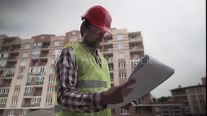 Builder reading blueprints on construction site. Under construction. Professional engineer architect in protective work clothing thoughtfully examines plan for the construction of residential area.