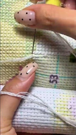 embroidering a colorful pattern cross stitch canvas using white thread and needle manually