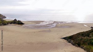 Taking off from a large golden sandy coast. Three cliffs bay, Wales. Aerial