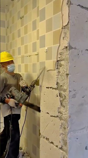 Worker demolishing tiled concrete wall using heavy electric jackhammer