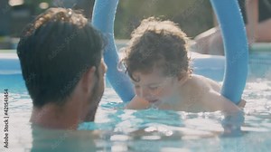 Father teaching son to swim on summer vacation in outdoor swimming pool using floatation aid - shot in slow motion