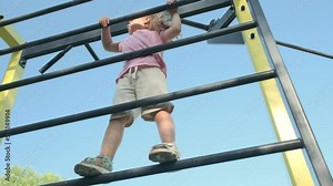 Little girl climbs gymnastic ladder on open sports ground on outside. Cute little girl crawls on vertical sports ladder in city park on sun day. slow motion