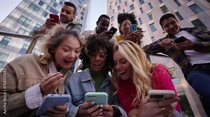 Group of young people watching something at phone sitting on stairs. Smiling multicultural friends looking social media outside the university campus. Students in their free time.
