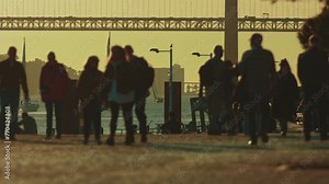 People walking beach near bridge at golden hour