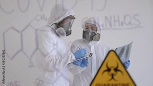Two doctors in medical protective suits examine a chest x-ray in a hospital room for isolated patients. Treatment of COVID-19 virus. In the foreground is a glass Board with the formula.