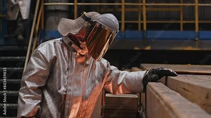 A man in a fireproof suit stands in the smelting shop of a metallurgical plant.