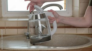 Woman pouring filtered water into glass electric kettle. Kitchen faucet. Sink with two taps, plain and filtered water. Filter system or osmosis, water purification. 4K video.