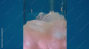 Slow motion close-up of Ice Cubes falling into an empty transparent Glass.The juicy orange carbonated beverage is poured into a glass with ice. Slow motion macro. Background blue. Barbie core. Barbie