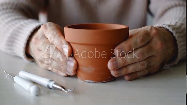 Hands cradling a small terracotta pot with sculpting tools on a table person woman
