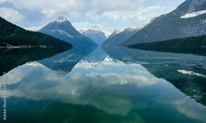 Pan with reflections: A calm, glassy lake with reflections of the surrounding mountains. The camera pans across the surface of the lake, highlighting the perfect reflections and the clarity of the wat