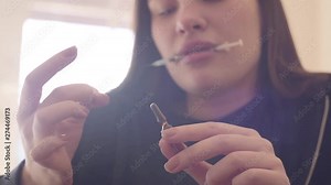 Portrait young bad looking woman preparing the syringe for injection close-up. Addict girl opening the ampoule holding syringe in her mouth. Troubled teens. Drug addiction. Bottom view. Slow motion