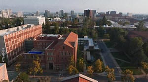 Aerial view of UCLA campus bathed in golden light, showcasing Romanesque Revival and Gothic architecture amid lush greenery, with Royce Hall as the centerpiece.