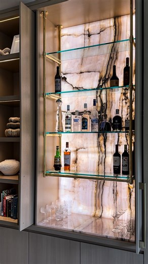 Devon Grace Interiors | Design x Build on Instagram: "A secret worth keeping… and revealing. 🥂 This concealed bar opens to a stunning Pink Onyx slab, floating brass-and-glass shelving, and a full LED backlight that makes this hidden bar glow like artwork. Closed for a clean look. Revealed for maximum impact 🙌🏼 Design: @dgi_designbuild Project: #DGIHiddenGem"