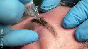 Microblading tattoo , permanent make-up. The master in gloves, using a special needle, injects pigment into the skin and colours the eyebrows with the hair technique, close-up view