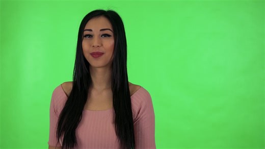 Young attractive asian woman points to camera - green screen studio | Premium Stock Video Footage