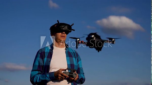 Man piloting drone with fpv goggles and handheld controller against blue sky with cloud, showing pilot control and remote flight operation, focused drone flight, fpv view and outdoor hobby activity Stock Video