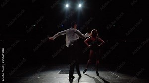 Ballroom dancers pair on concert hall stage,rear view.Slow motion synchronous dance movements and ballroom steps with hip swinging,arm swings,bends.Expressive couple dance fragment.Black and white .