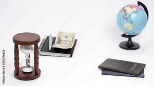 Spinning globe, hourglass, notebook, money, passports, tickets and a toy airplane on white background. Stop motion animation.