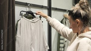 Woman in fitting room prepares to try on selected clothes She inspects each clothes imagining how about. She immerses herself in world of clothes carefully considering each piece before final choices.