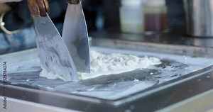 Making ice cream rolls on cold plate - chopping up cream and raspberries