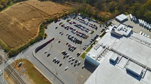 Many associate cars parked on big parking lot in front of industrial factory building. Manufactoring and global industry concept