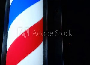 An old-styled barber shop sign, symbol. Round pole light in dark. Old-fashioned rotating led red white blue stripes pole light near men hair salon. Advertise of a small business outdoors. Hairdresser.