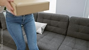 A young blonde woman smiles while unboxing a package in a contemporary living room, depicting a relatable indoor scene of receiving goods.