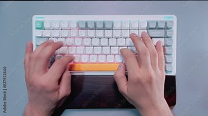 Typing on White Mechanical Keyboard with RGB Lights. Top view of hands typing on white keyboard with RGB LED lights.
