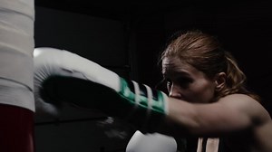 Female fighter during an intense boxing workout throws strong and fast punches on a punching bag with precision