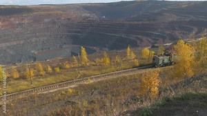 The movement of a train transporting iron ore through a huge quarry with machines and excavators working in it. The clip is in 4k resolution, with sound.