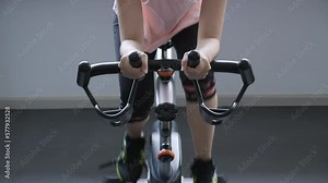 Front view close-up shot of unrecognizable Asian woman, exercising, sprinting, using indoor cycling machine, workout alone. fitness gym, sport, health, wellbeing, weight loss, cardio workout concept