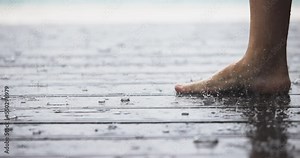 Women's barefoot covered in droplets of heavy rain in close-up. Caucasian Female legs walking on the wet wooden floor in rain weather. Happiness calmness concept. Slow motion