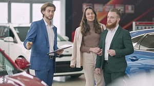 Young wealthy couple consulting dealer in showroom. Portrait of positive rich confident Caucasian man and woman talking with employee in car dealership choosing new vehicle.
