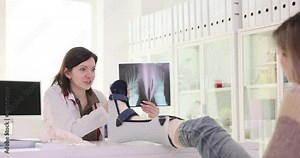 Traumatologist shows X-ray picture of patient feet and in clinic office slow motion. Doctor woman performs injury recovery process in hospital