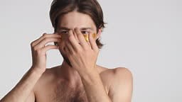 Attractive brunette guy happily applying gold patches under eyes over...