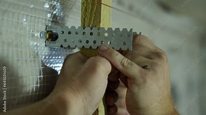 A worker installs a frame of beams and metal fasteners for installing OSB on a wall indoors. Close-up