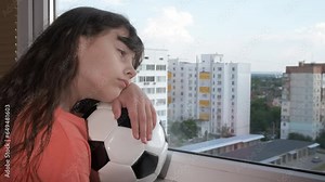 Look through window with ball. A little girl hold the ball and look through the window. A concept of quarantined time during childhood.