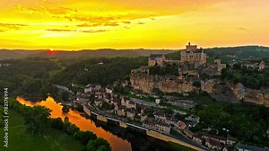 Cinematic panoramic view of feudal square-shaped castle on a riverside clifftop at golden sunset in France. Aerial view of Château de Beynac fortress at golden hour in France.
