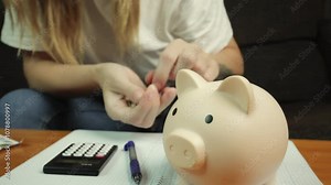 Woman sits at table, calculating expenses with calculator, pen, and notepad. Coins added to piggy bank, illustrating personal finance and budgeting practices