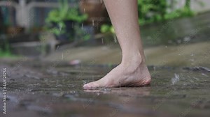 After raining activity, close up barefoot slowly stomping in water puddles on a paving cement footpath, tropical rainy season, climate changes, environmental issue, adult having fun with playing water