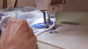 A seamstress uses a universal sewing machine with a special foot to lay a finishing stitch along the neck .