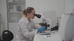 Female medical professional works with samples and analyzes in medical laboratory behind microscope. Woman lab technician analyzing sample through microscope in hospital. Medicine, microbiology.