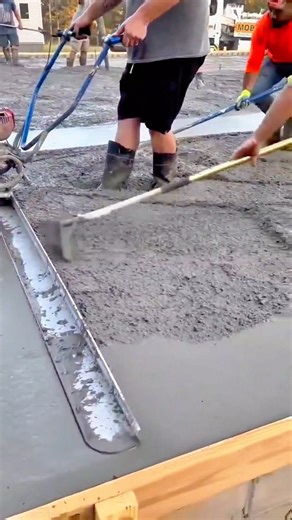 Construction workers pouring and leveling wet concrete slab using a motorized power screed