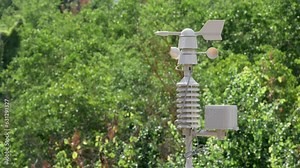 Weather vane and wind sensor of a weather station moving by the action of the air on a sunny and windy day and a blanket of out-of-focus tree leaves in the background