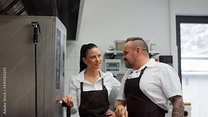 Chef teaching cook how to use combi oven indoors in restaurant kitchen.