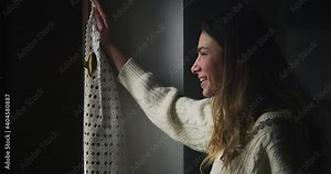 Cinematic shot of young happy smiling woman opens curtain looking through window greeting and sending air kiss with love to her husband back from work. Concept of hope, happiness, marriage, surprise.