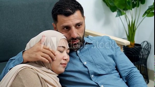 Caring husband comforts his wife with gentle embrace while watching tv using remote at home